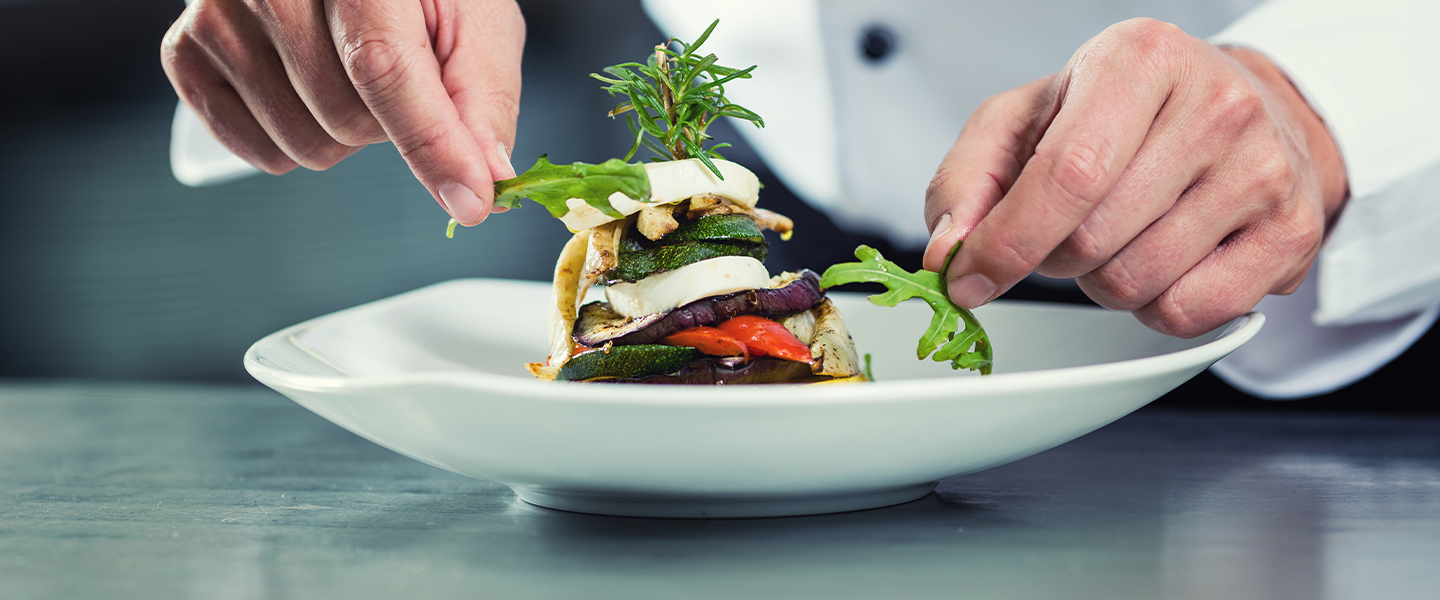 Manos de chef colocan verduras frescas en un plato, destacando los ingredientes de un proveedor de alimentos como Nestlé.