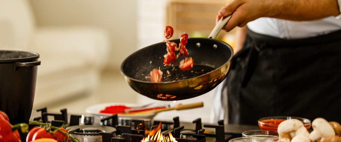 Manos salteando tomates con otros productos culinarios en una sartén sobre estufa