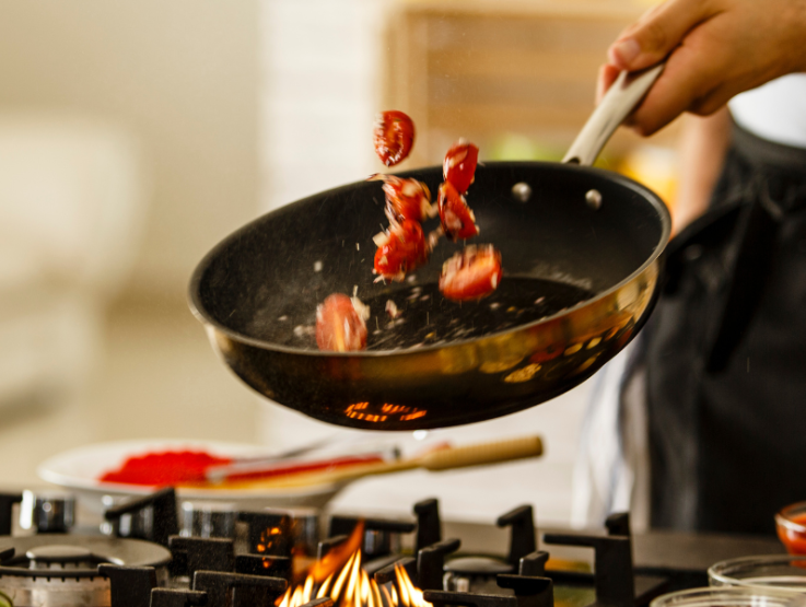 Manos salteando tomates con otros productos culinarios en una sartén sobre estufa