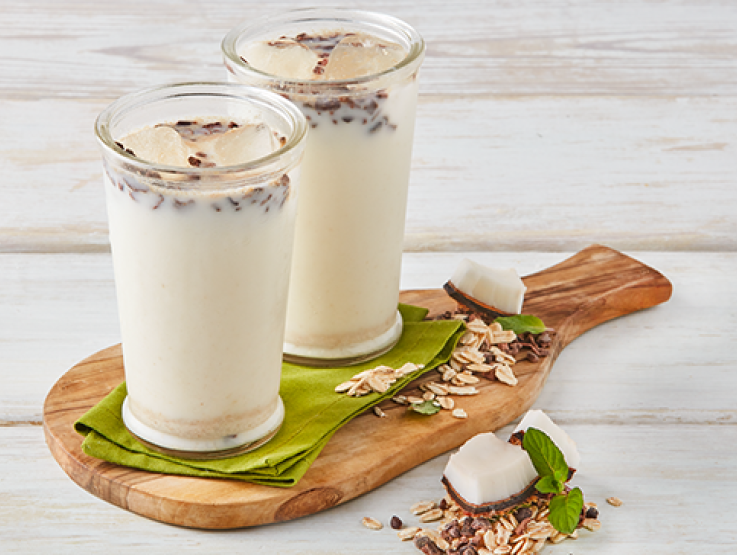 Dos vasos con agua de avena con coco sobre tabla de madera
