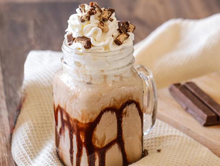 Vaso de malteada de chocolate y decorado con crema batida y trozos de KITKAT® 4 Fingers