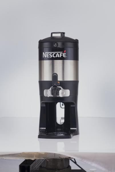 Dispensador de máquina NESCAFÉ® Boxha con exterior metálico y negro sobre fondo oscuro.