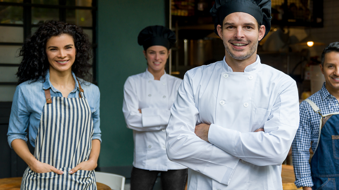 Dos chefs y dos meseros con uniformes sonriendo