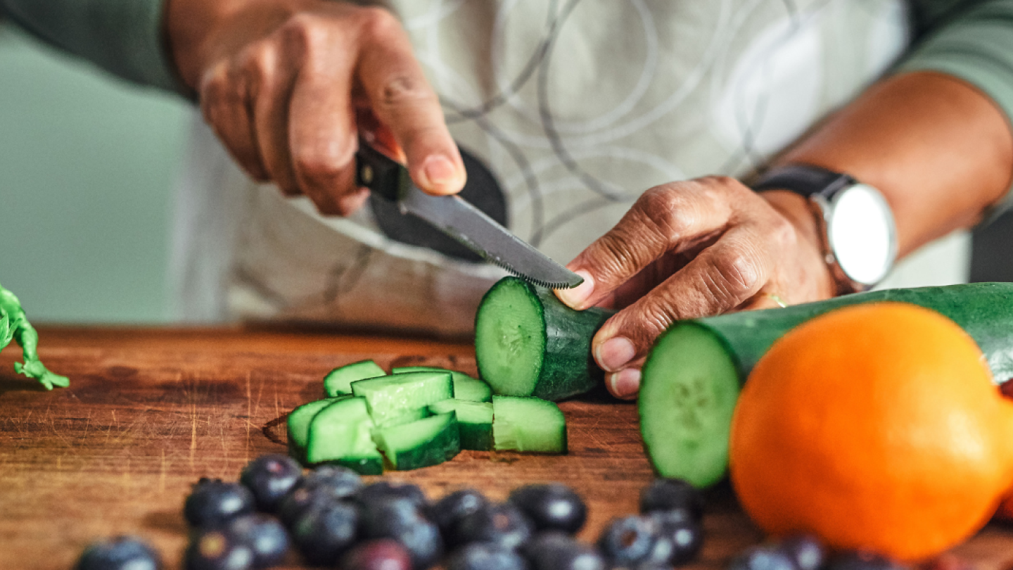 Manos de hombre cortando un pepino junto sobre una tabla de madera