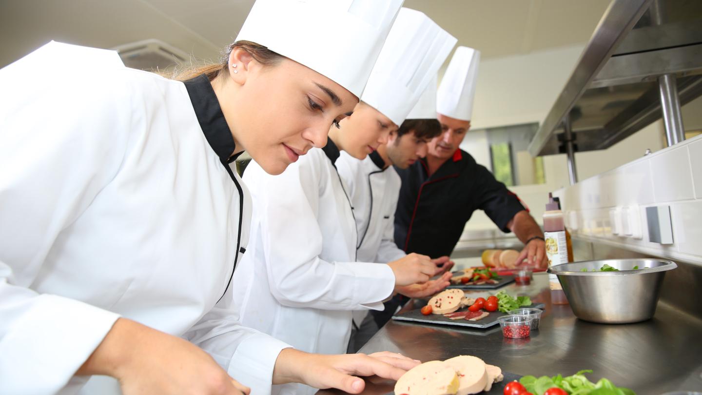 Tres jóvenes estudiantes de gastronomía junto a su instructor dentro de una cocina