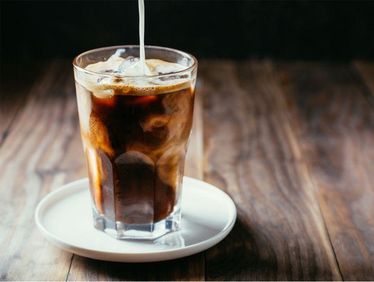 Vaso de café frío con hielo y bebida vegetal servido sobre una mesa de madera