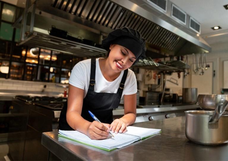 Chef escribiendo en una libreta dentro de una cocina industrial durante una jornada de formación