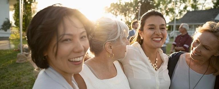 Grupo de mujeres abrazadas sonriendo al aire libre durante una actividad comunitaria