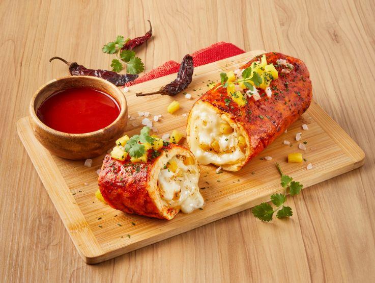 Rollos rellenos con queso derretido y salsa roja, decorados con hierbas sobre una mesa de madera